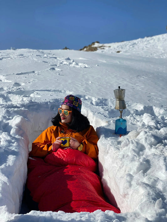 Woman enjoying the deep snow in a downfilled sleeping bag on a sunny day